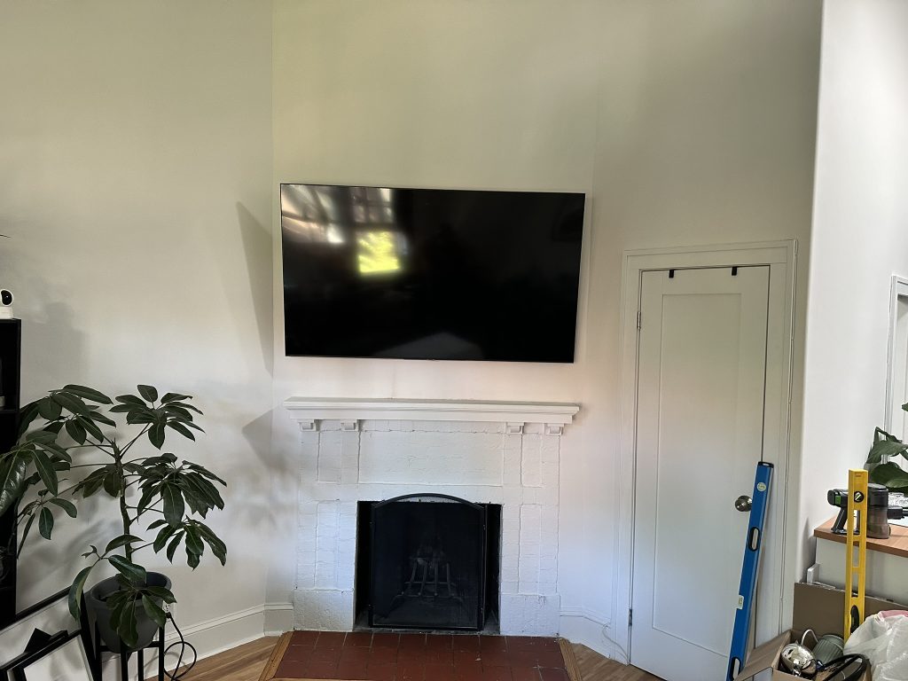 65 inch Samsung OLED TV mounted on a full motion bracket above a white brick fireplace with hidden wiring in Westbury, NY