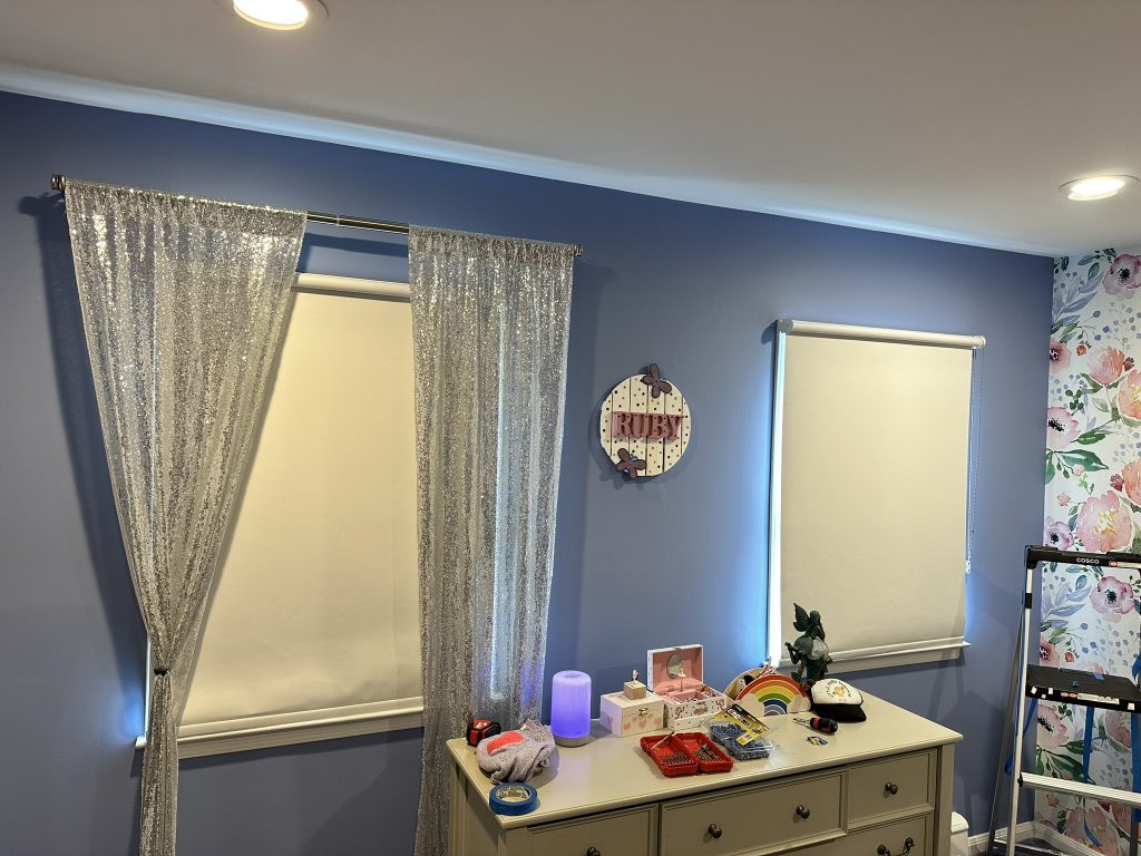 Custom window treatment sequin drapes and roller blinds installed in a blue child’s room in Great Neck, NY