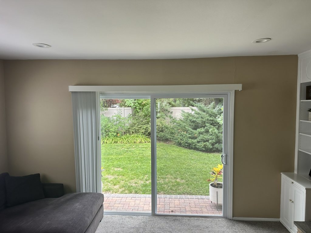 White vertical blinds installed over a sliding glass door in a living room in Oyster Bay, NY
